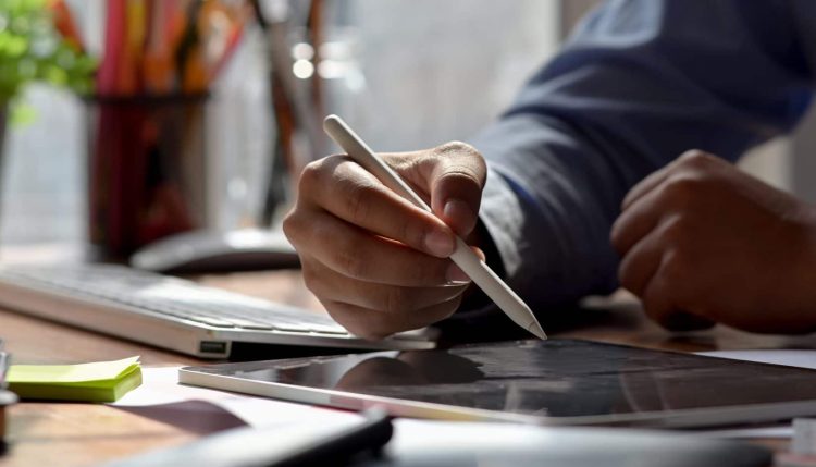 Close up view of graphic designer drawing on digital tablet with stylus and designer supplies on wooden worktable